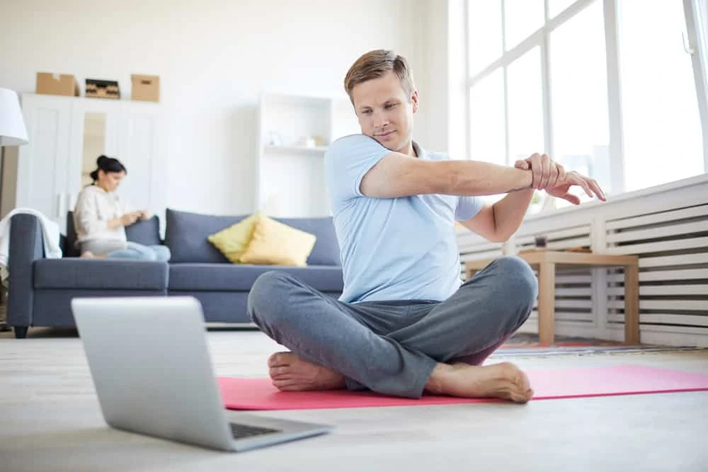 Mann im Wohnzimmer macht eine sportliche Übung vor dem Laptop