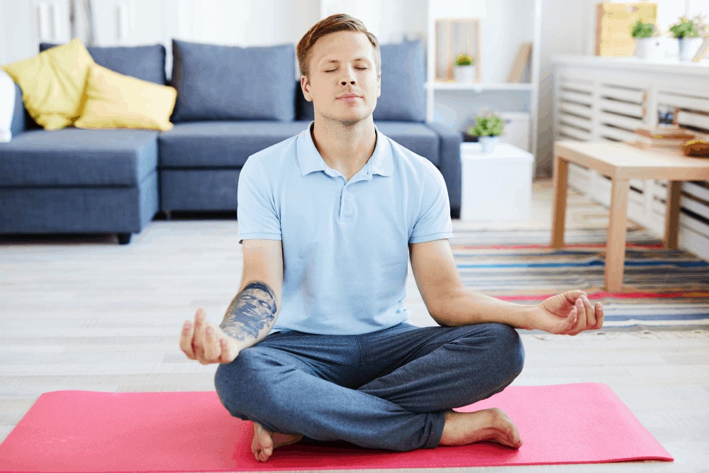 Ein Mann sitzt in Meditationshaltung auf einer Yogamatte