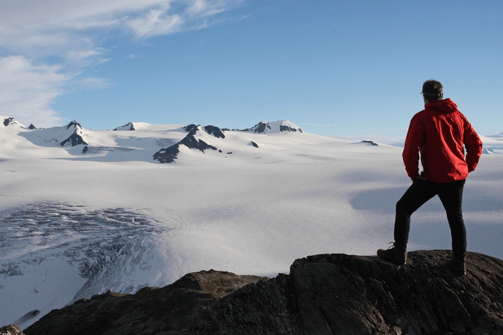 Ein Mann Steht auf einem Berg und schaut auf ein verschneites Gebirge
