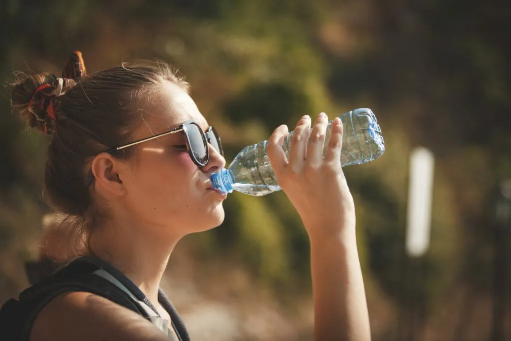 Das Bild zeigt eine Frau, die Wasser trinkt. Jetzt Tipps gegen Hitze entdecken.