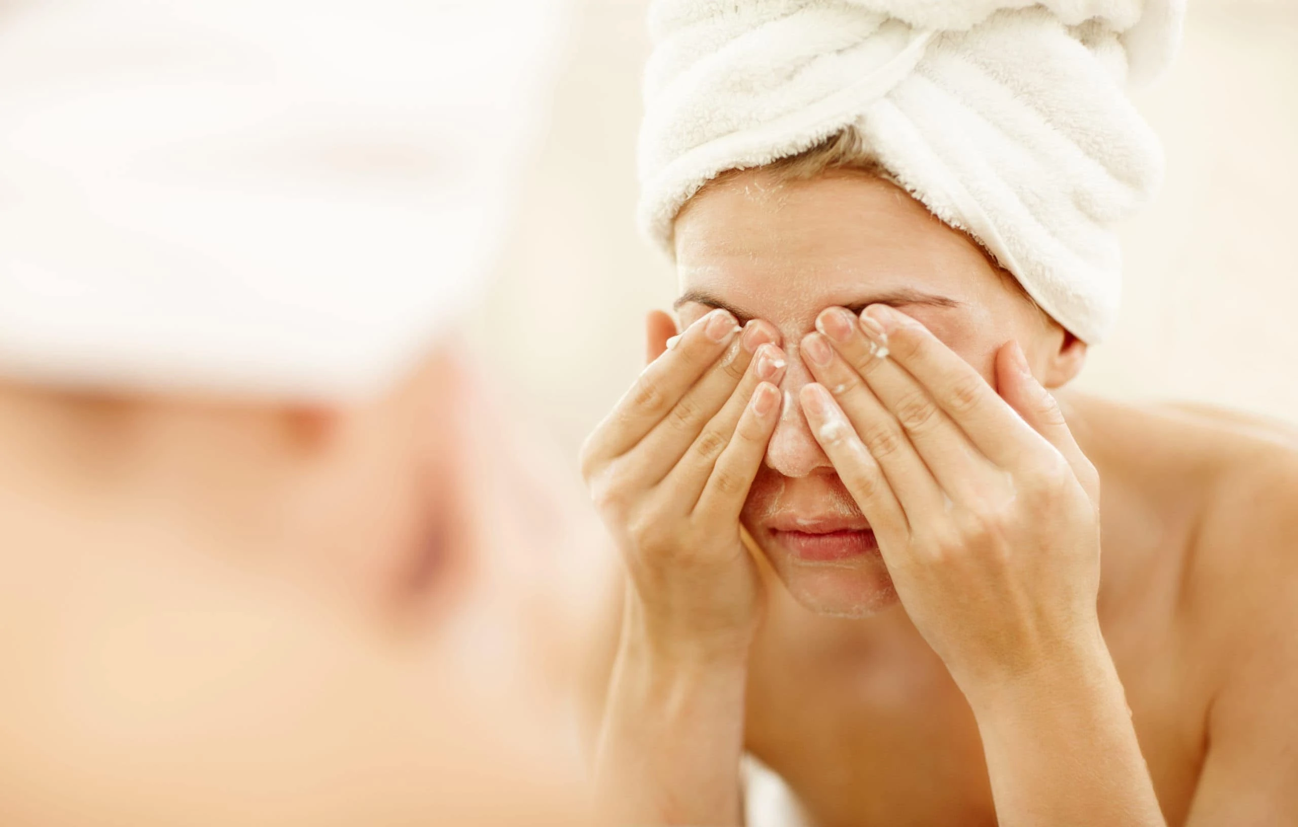 Eine Frau mit Handtuch auf dem Kopf wäscht sich das Gesicht