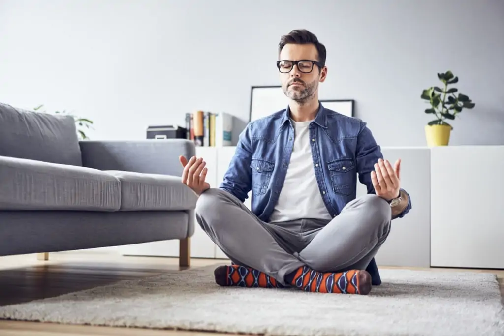Ein Mann meditiert zuhause, um die Folgen von Stress zu minimieren