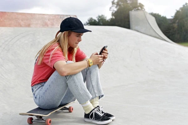 Skateboarderin sitzt am Handy und hat FOMO