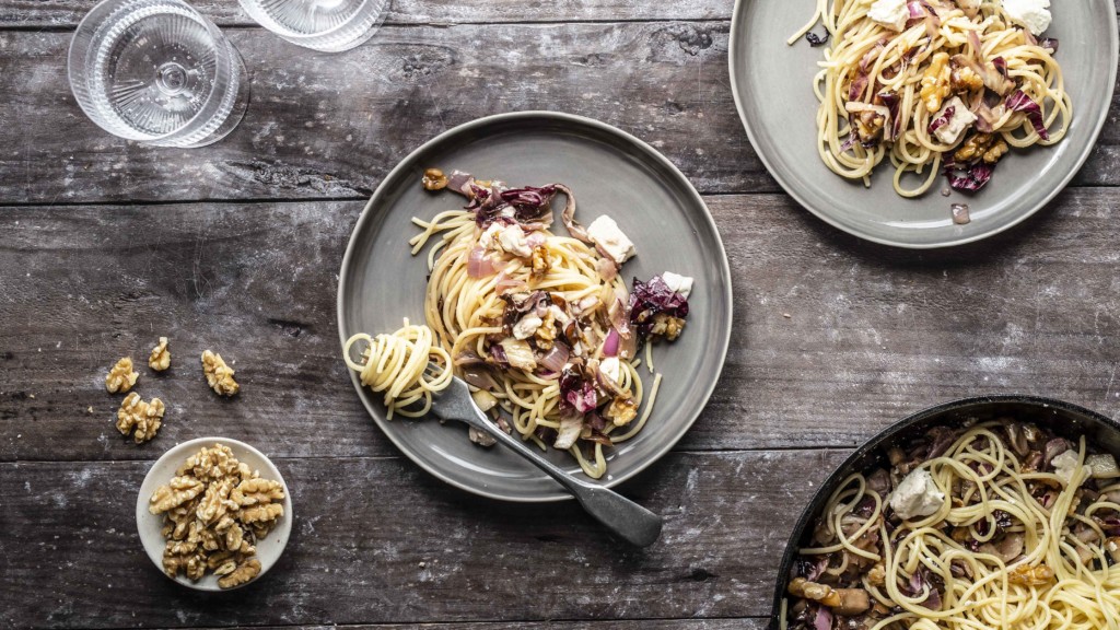 Auf zwei Tellern liegt jeweils eine Portion Spaghetti mit Radicchio und Walnüssen. Auch eine Pfanne mit der Radicchio-Pasta ist zu sehen.