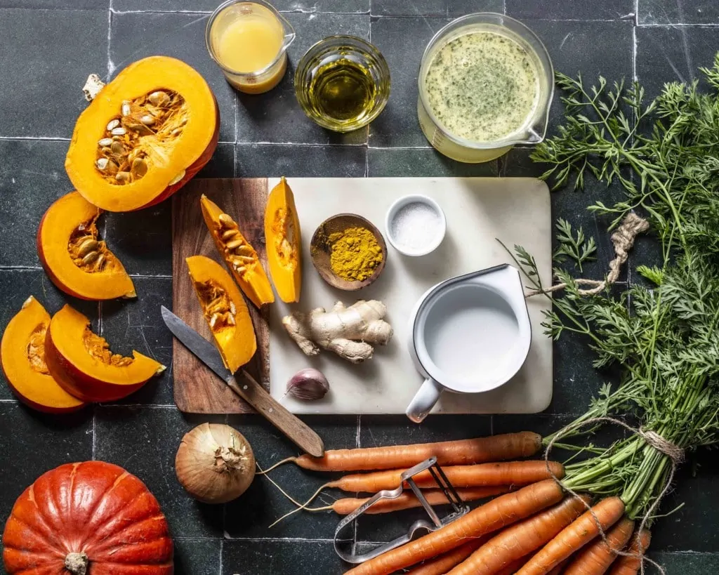 Auf einer Küchenzeile liegen alle Zutaten für die Kürbissuppe mit Orangensaft und Kokosmilch bereit.