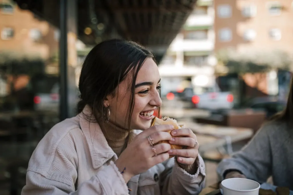 Eine junge Frau isst einen Burger; sie fühlt sich wohl dank der Ernährungsberatung