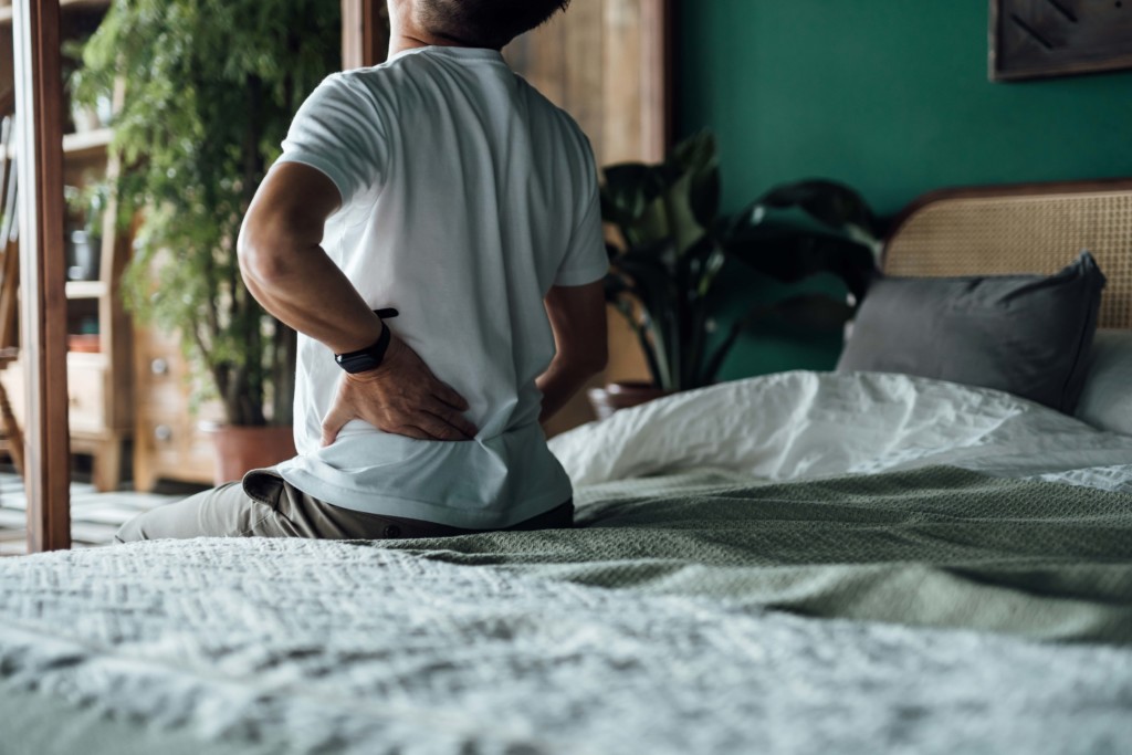 Ein Mann hat Rückenschmerzen durch Stress und sitzt auf dem Bett