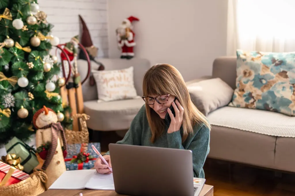 Frau plant mit Laptop und Telefon vor, um Weihnachtsstress zu vermeiden