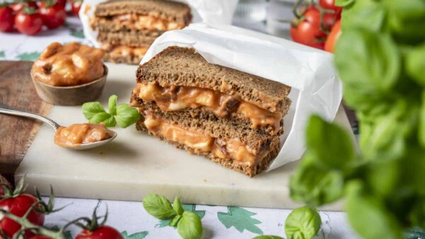 Auf einem Brett wird ein Pausenbrot mit einem Aufstrich mit getrockneten Tomaten und Mozzarella serviert.