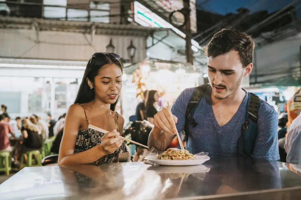 Das Bild zeigt zwei Personen beim Essen. Jetzt mehr über Krank im Urlaub erfahren.