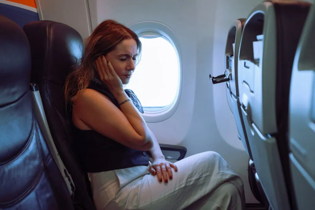 Eine Frau hat Ohrenschmerzen - sie hat Probleme beim Druckausgleich im Flugzeug