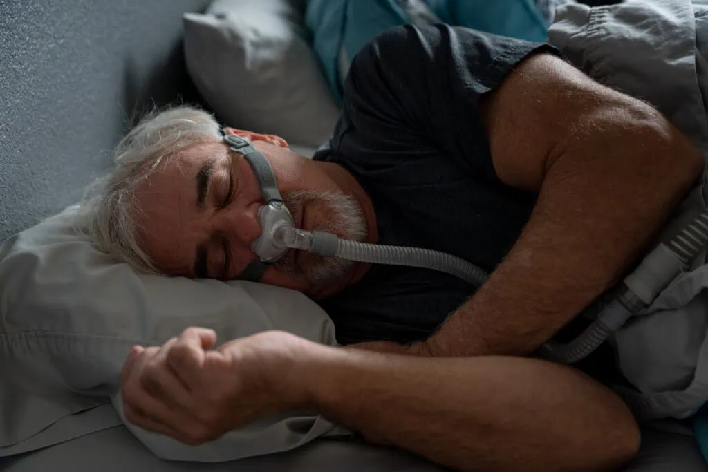Ein älterer Herr schläft - er nutzt dabei eine CPAP Maske zur Behandlung seiner Schlafapnoe