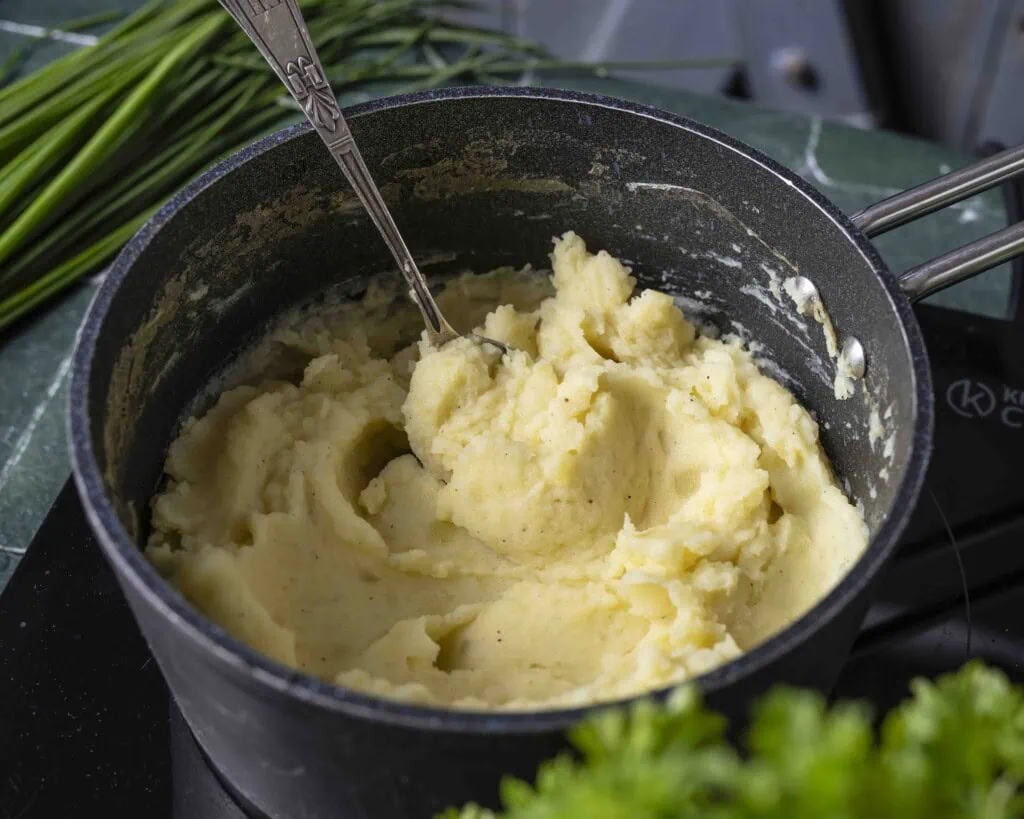 In einem Topf wird Kartoffelpüree mit einem Löffel umgerührt.