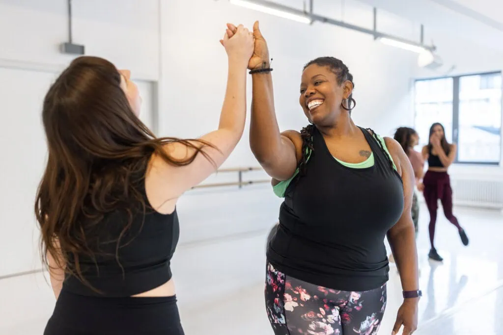 Zwei Frauen geben sich nach einer Bewegungseinheit ein High-Five – Bewegungstherapie bei Adipositas.