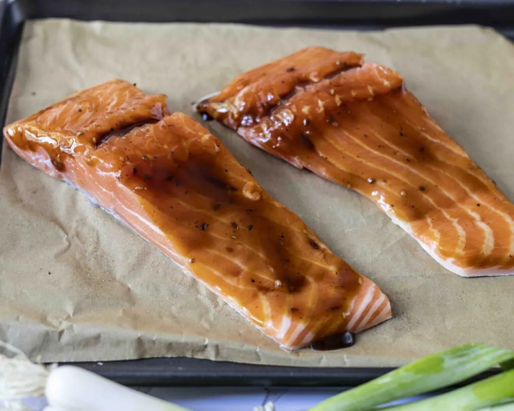 Der Lachs liegt auf einem Backblech und ist mit Teriyakisauce eingestrichen.