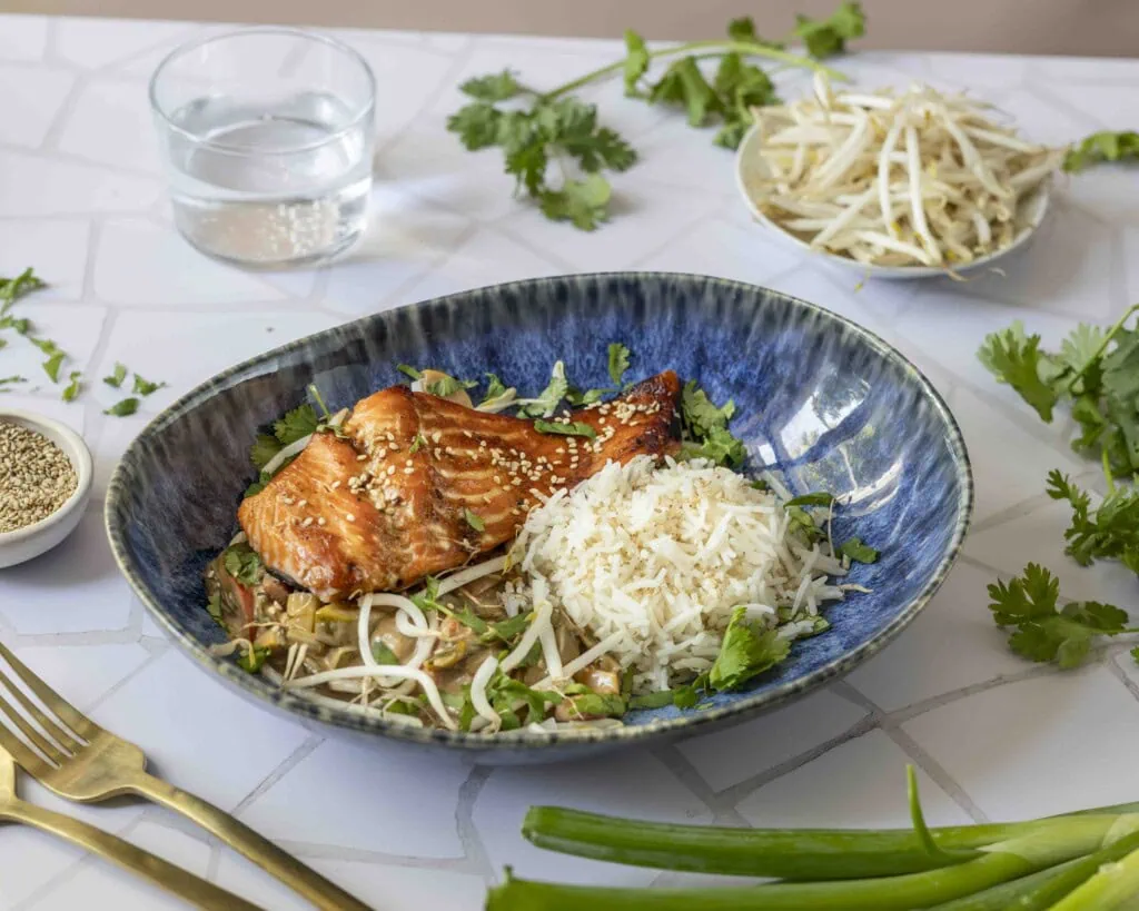 Lachs, Gemüsecurry und Klebreis sind auf einem Teller angerichtet.